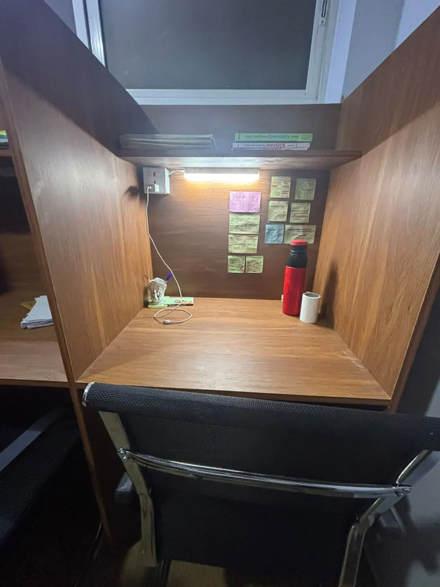 A wooden cabin desk with its own lamp, sticky notes and a water bottle.