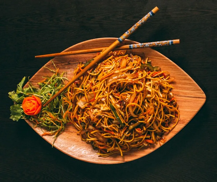 A plate of vegetable chowmein with chopsticks.